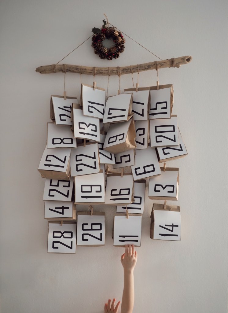 Adventkalender mit Säckchen die an einer Holzlatte gebunden sind.